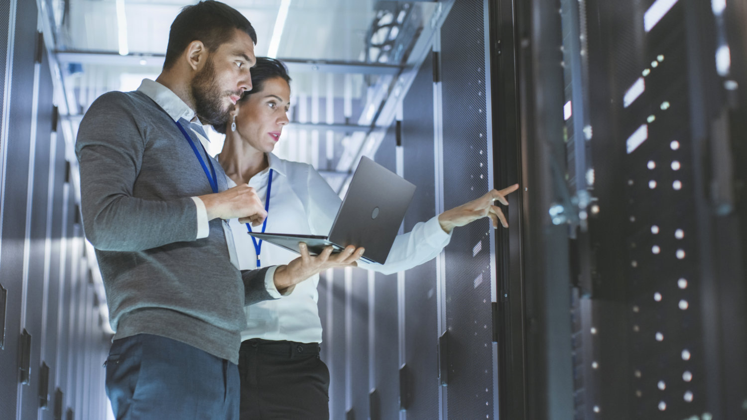 Male IT Specialist Holds Laptop and Discusses Work with Female Server Technician. They're Standing in Data Center, Rack Server Cabinet is Open